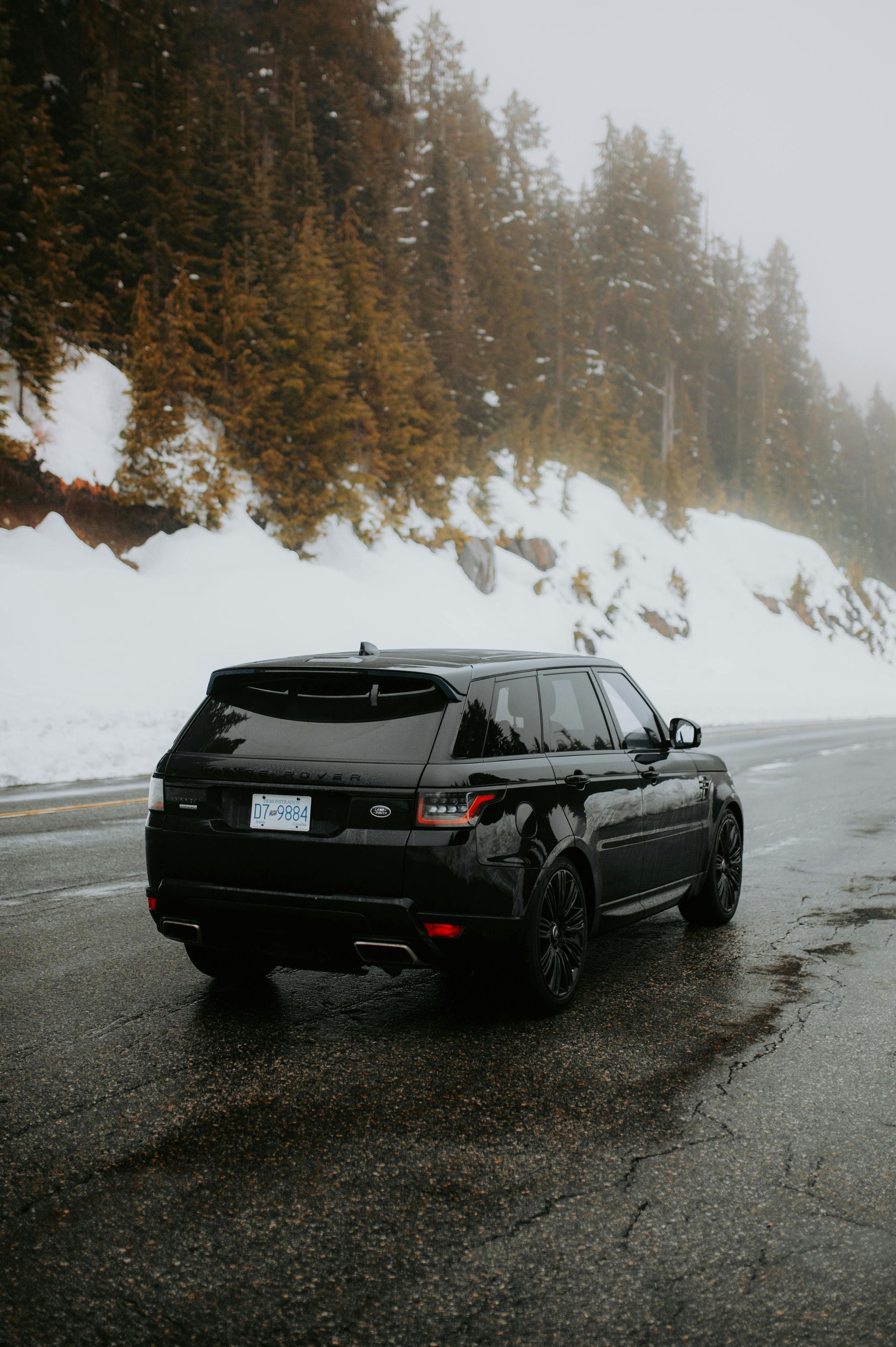 A black range rover is parked on the side of the road in the snow.