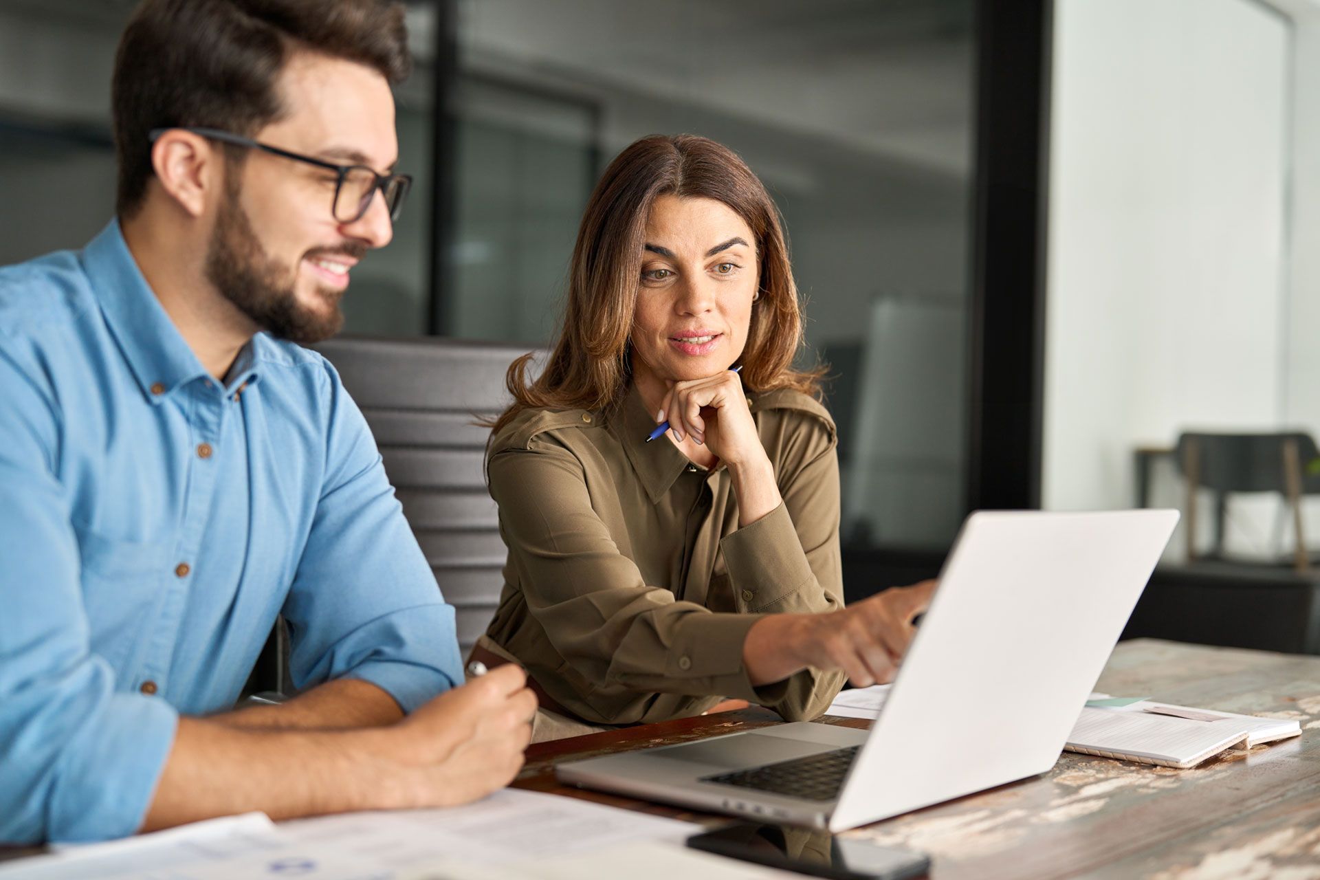 Two people looking at laptop, woman pointing; office setting.
