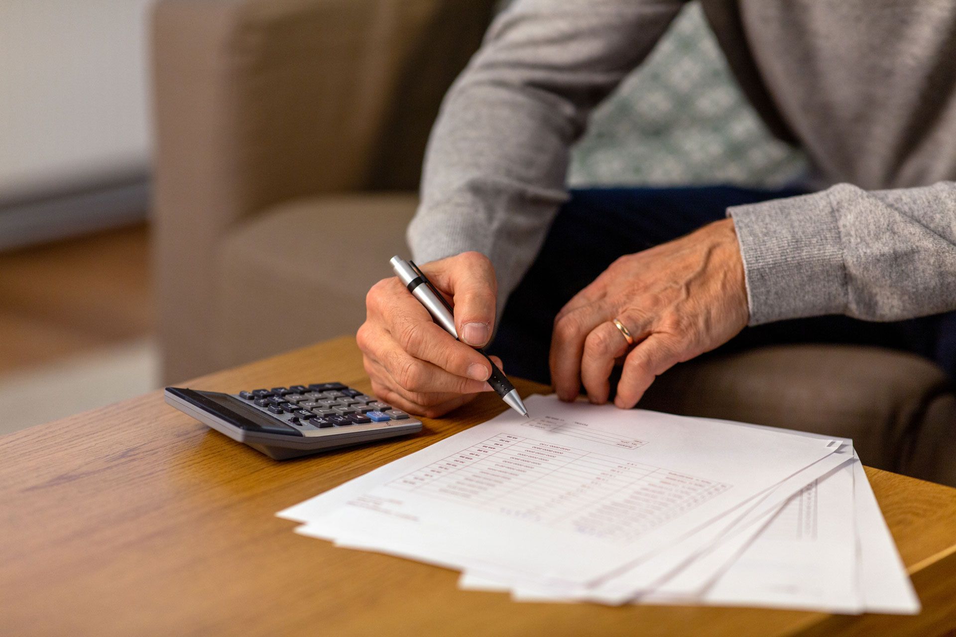 Person writing on papers with a pen next to a calculator on a table.
