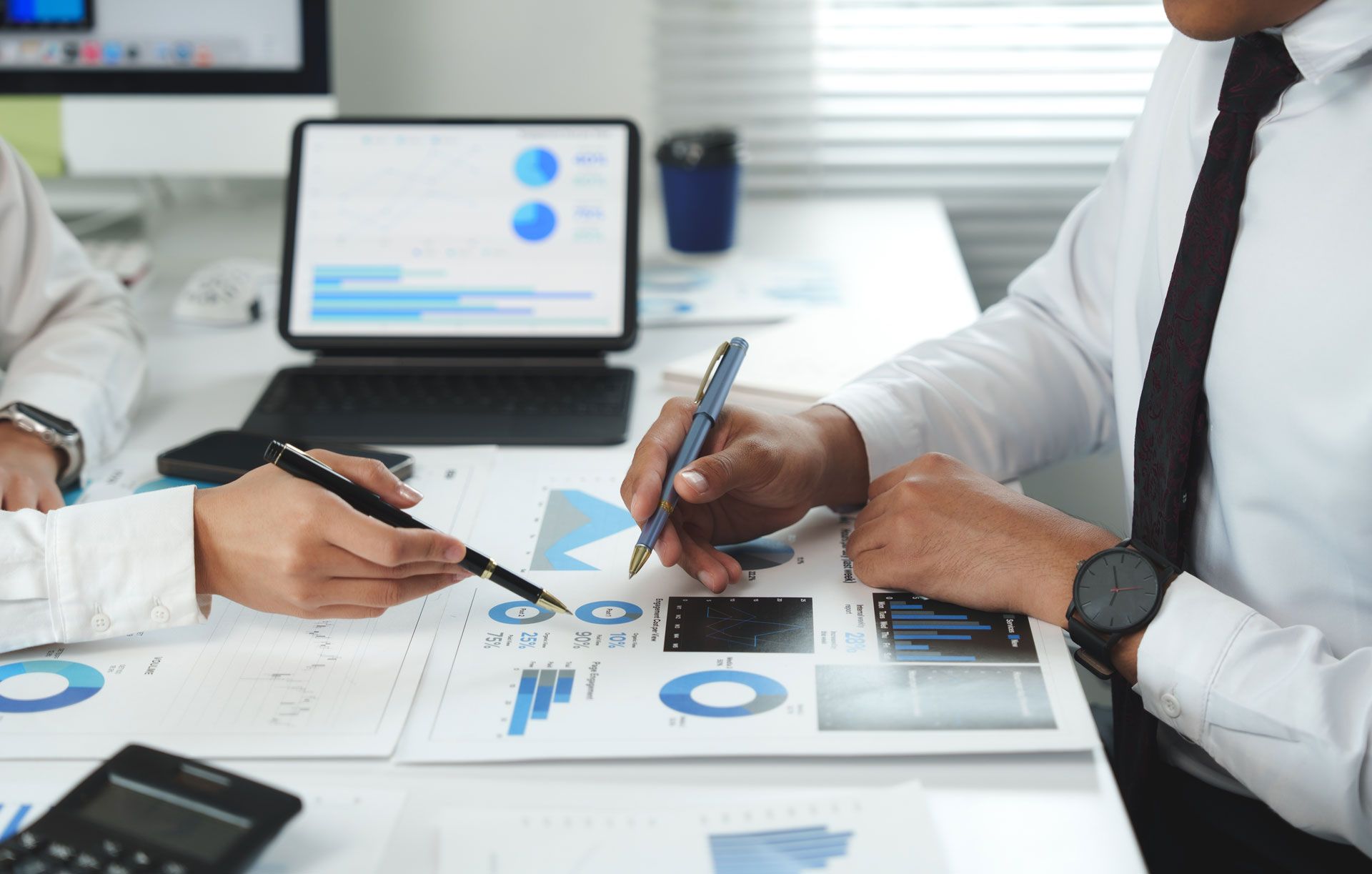 People reviewing financial data on paper and tablet, using pens to point at charts.