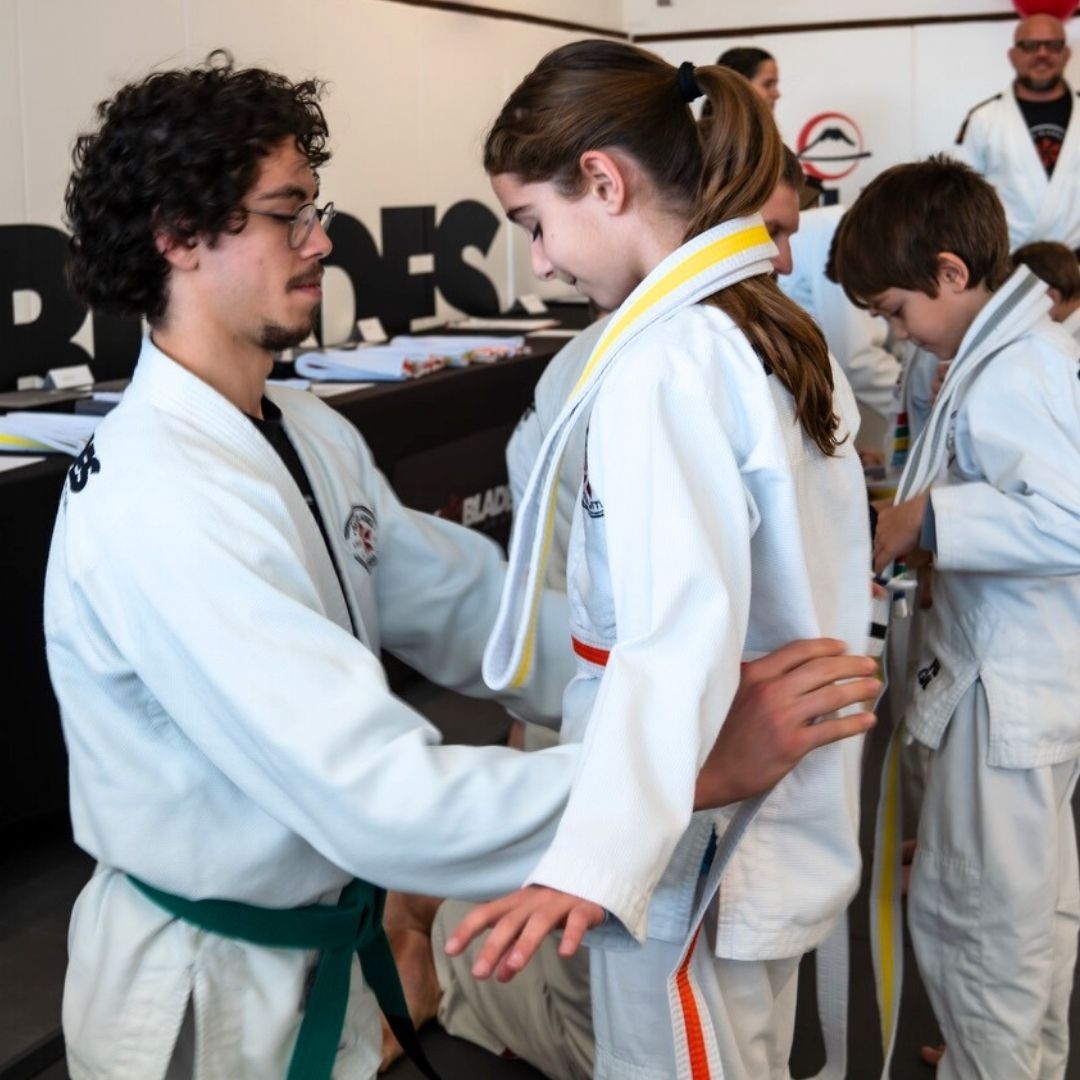 Two people grappling on a mat, one in a black gi, the other in a rash guard, legs entangled.