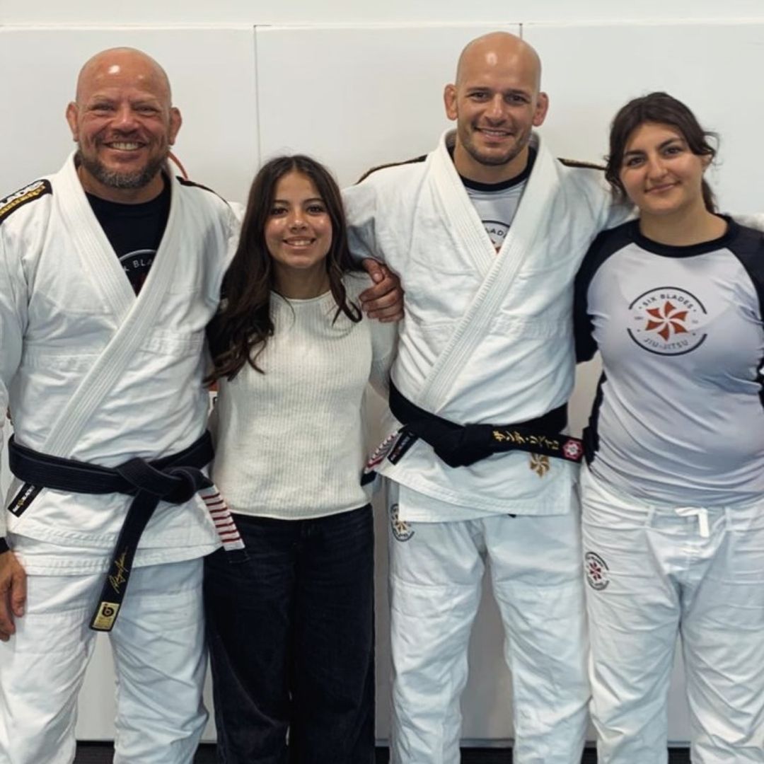 People practicing jiu-jitsu on mats, wearing gis in blue, black, and gray. Active grappling, gym setting.