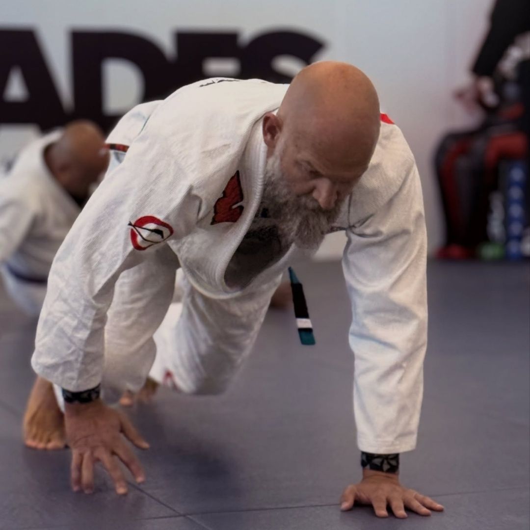 Two people practicing Brazilian Jiu-Jitsu on a mat; one in a black gi, one in a white gi, grappling.