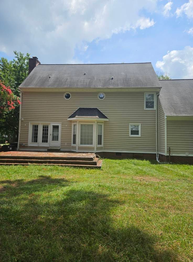 Back of a two-story beige house with a deck and yard. Blue sky with clouds visible.
