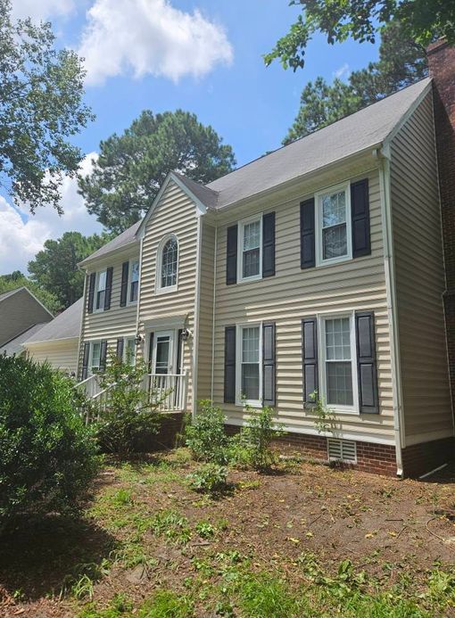 Two-story beige house with black shutters under a partly cloudy sky.