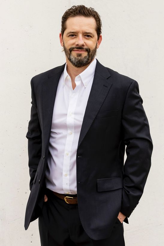 Derek is standing in a nicely tailored suit.