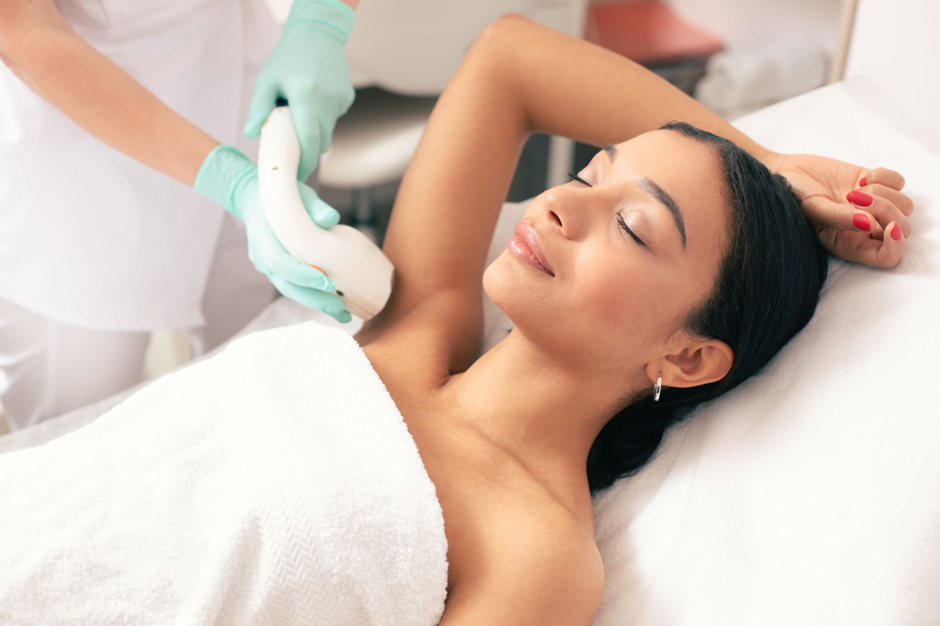A smiling woman is undergoing laser hair removal on her armpit at a medical practice.