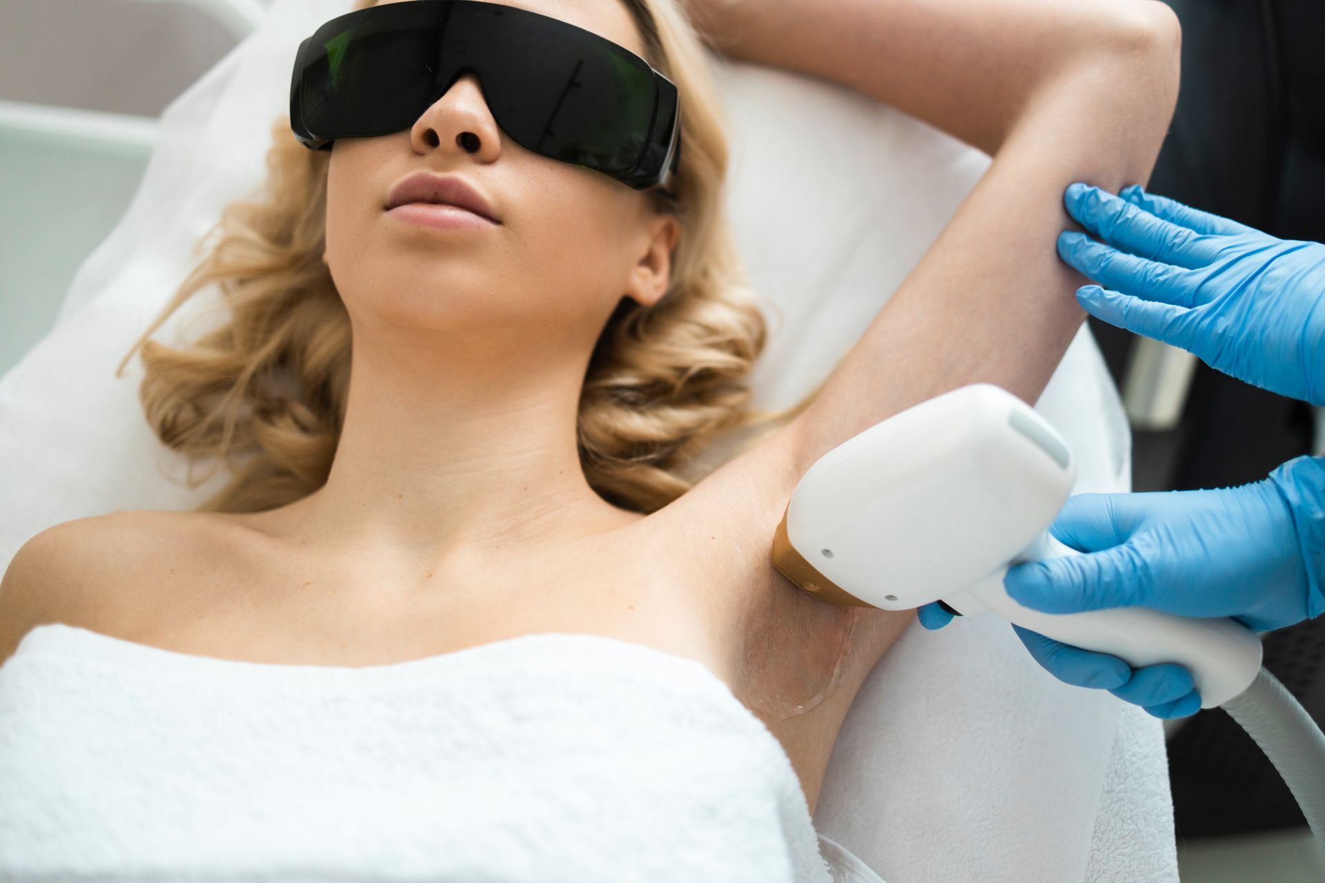 An individual performing laser hair removal on a client's underarm at a medical spa.