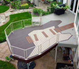Raised backyard deck with white railings, gray flooring, and built-in wooden bench seating attached to a house.