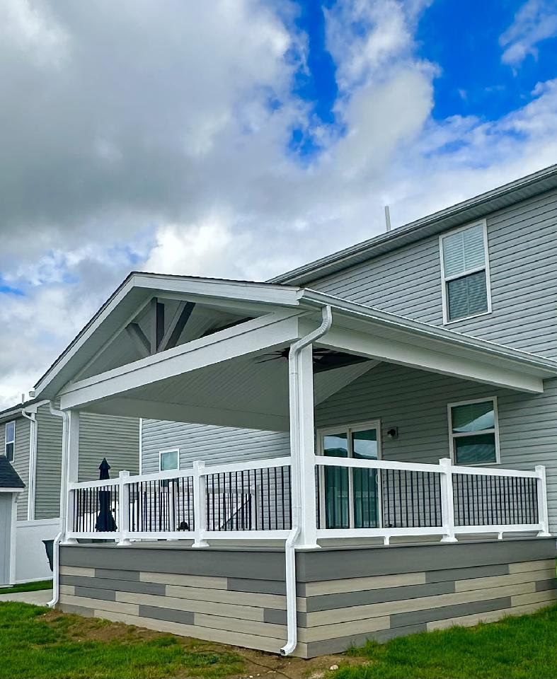 White house with a covered porch, white railing, and gray siding under a cloudy blue sky