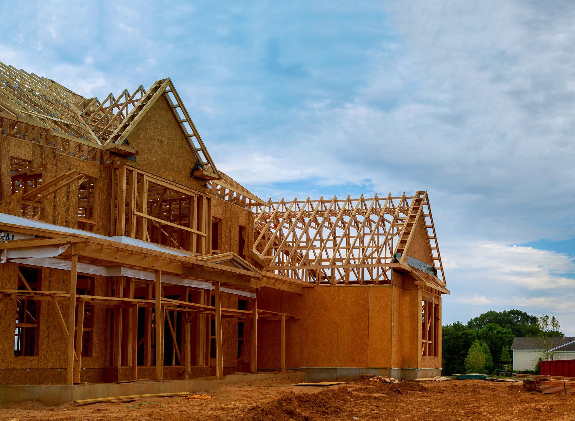 Wooden house under construction with exposed framing and a cloudy blue sky