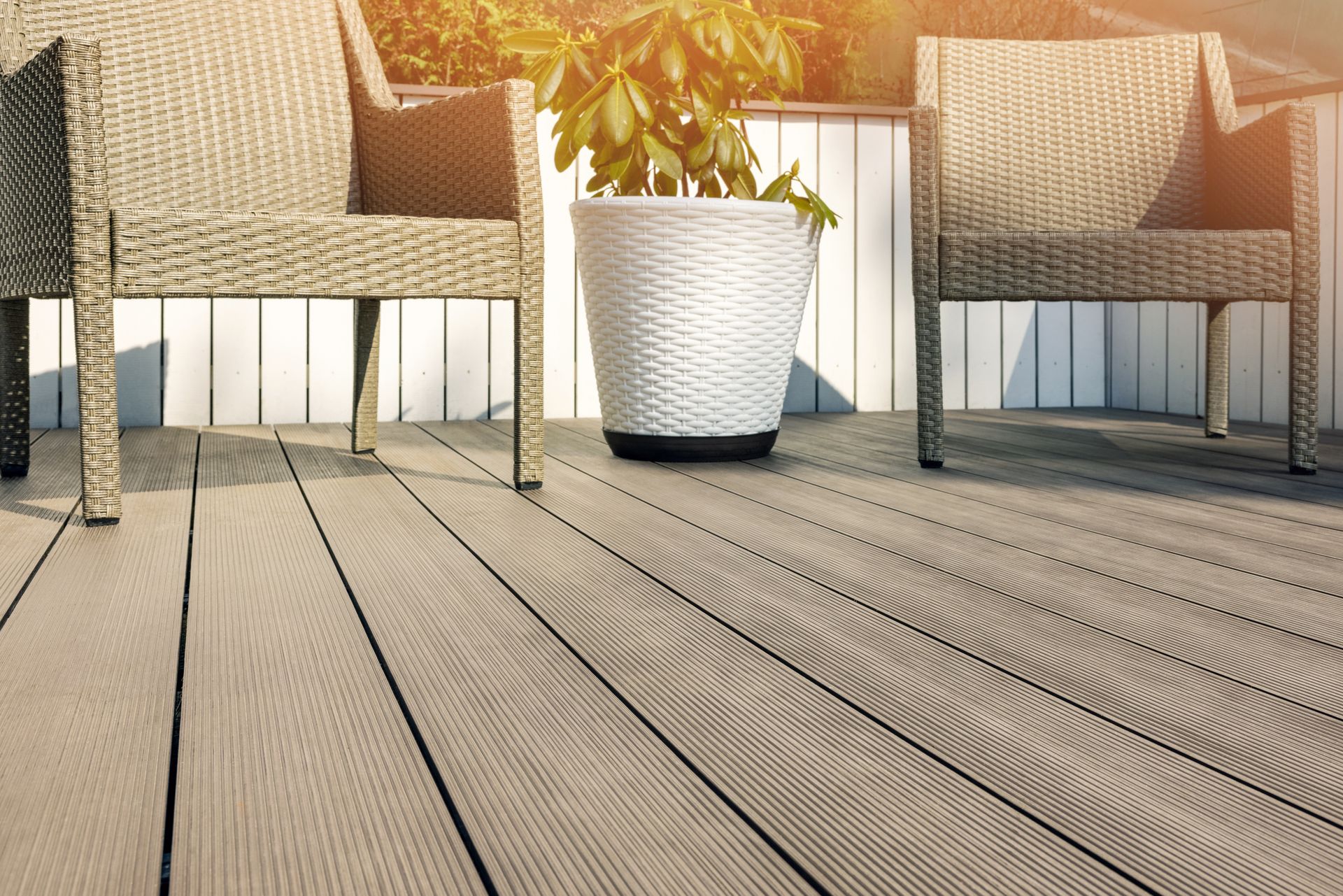 Sunlit patio with two wicker chairs and a white potted plant on a wooden deck