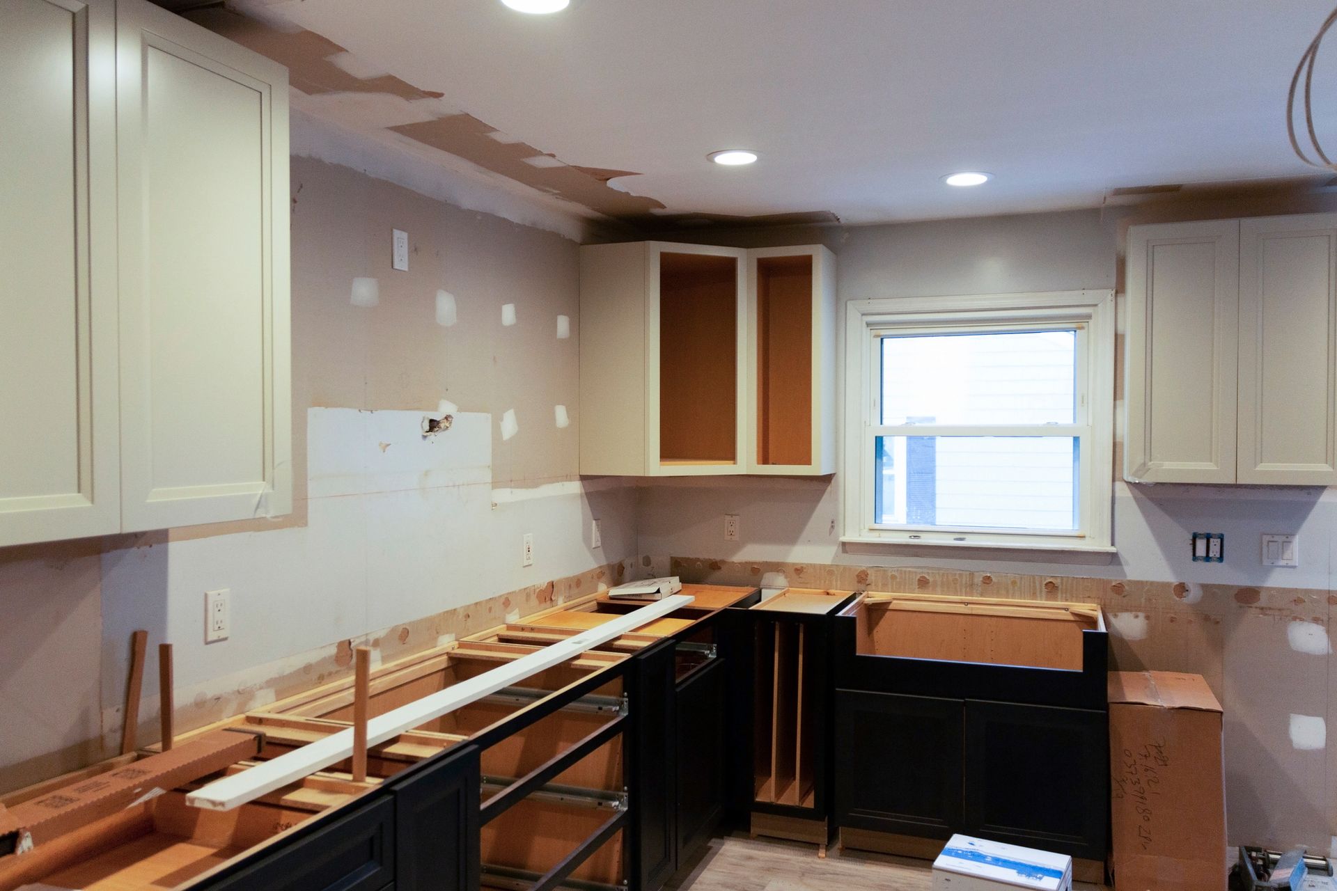 Partially renovated kitchen with unfinished cabinets, exposed counters, and a window over the sink.