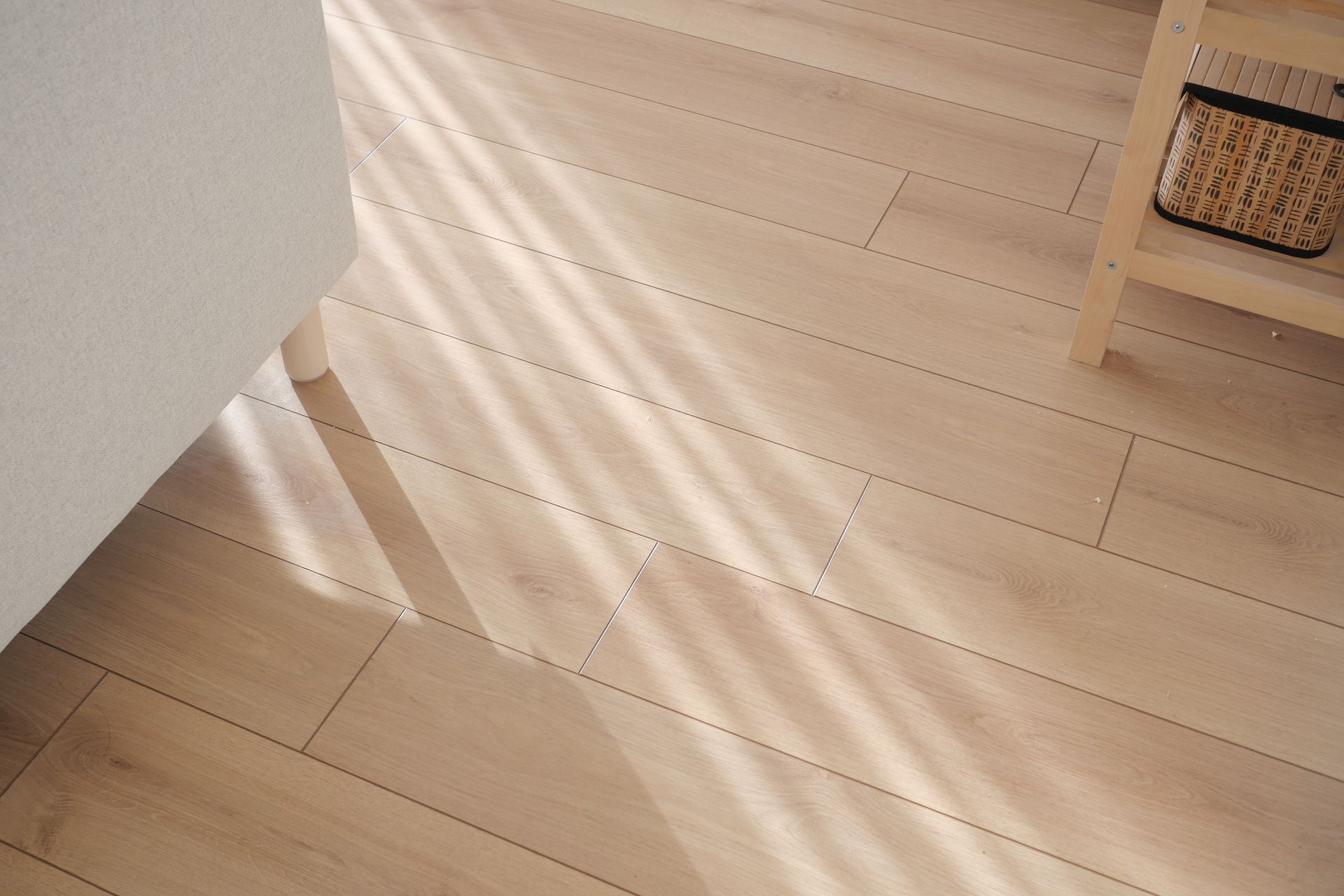 Sunlight streaming across a light wood floor beside a white wall and woven basket shelf
