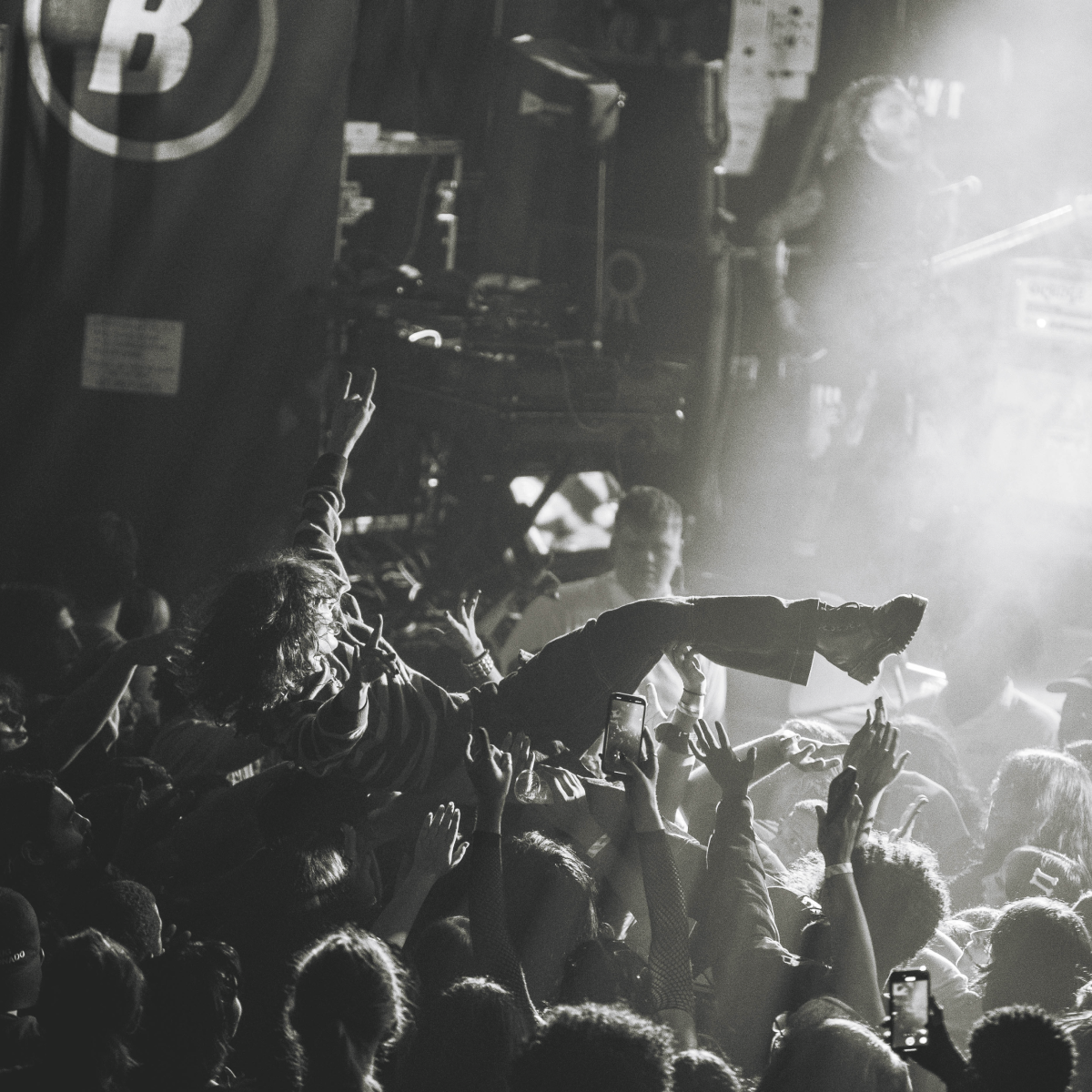Person crowd-surfing at a concert. Arms raised, lit by spotlights and flanked by a cheering crowd.
