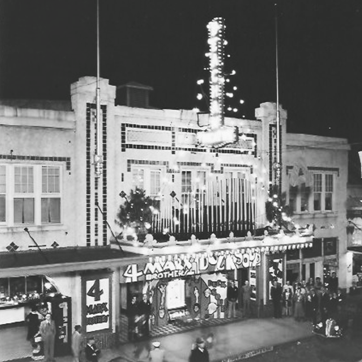 Exterior view of the historic Beacham at night. Decorated facade and marquee; people gathered below.