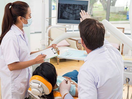 A dentist and a nurse are looking at an x-ray of a patient 's teeth.