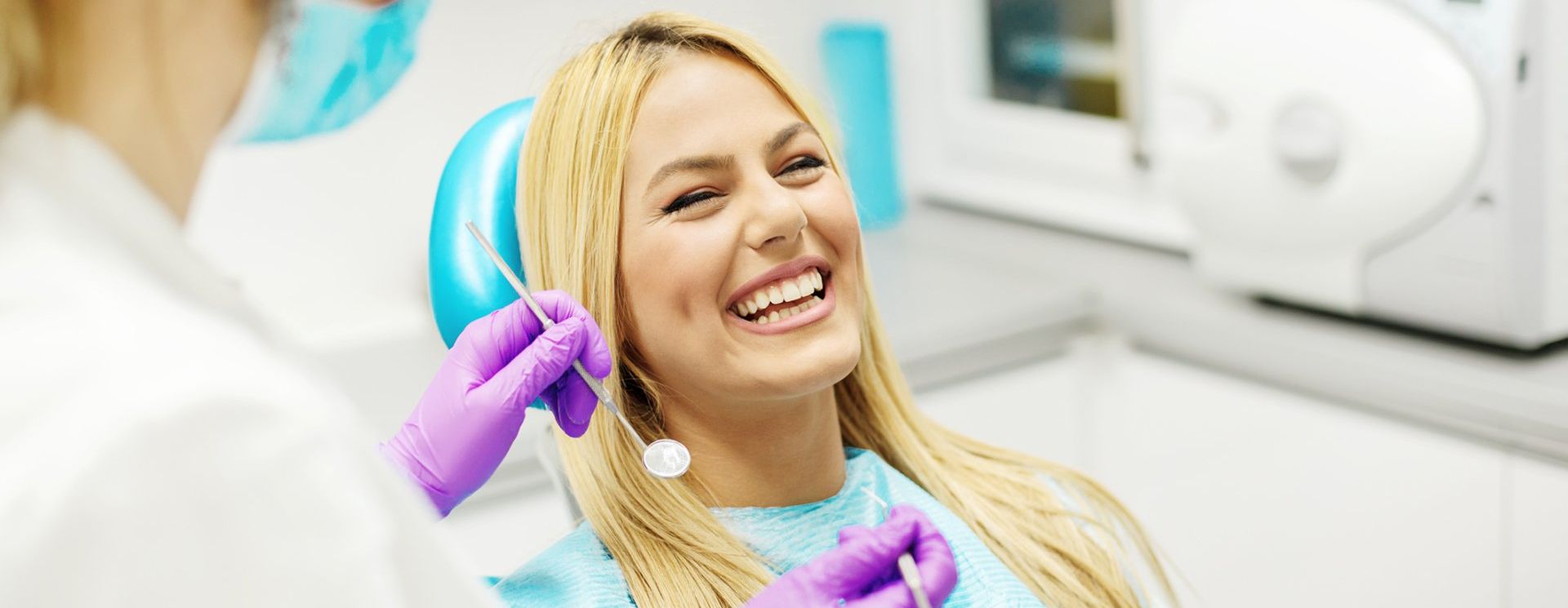A woman is smiling while sitting in a dental chair.