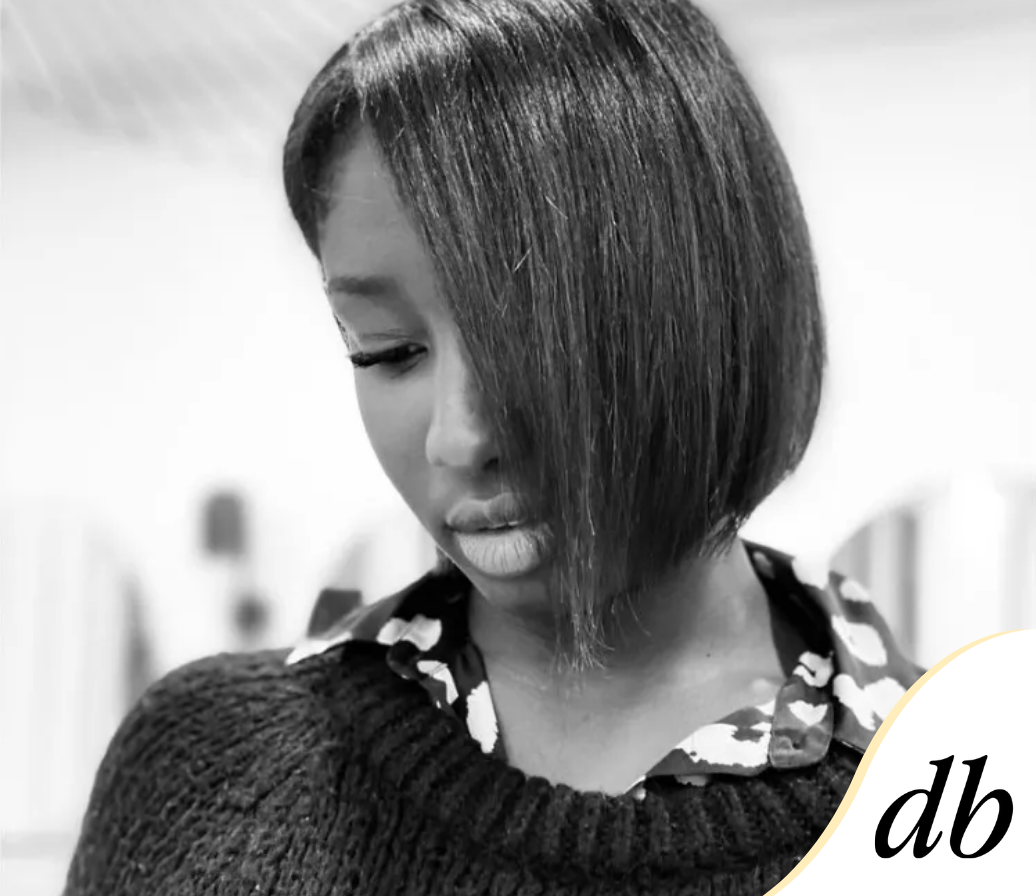 Femme aux cheveux courts et foncés, regardant vers le bas, portant un pull sur une chemise à motifs.