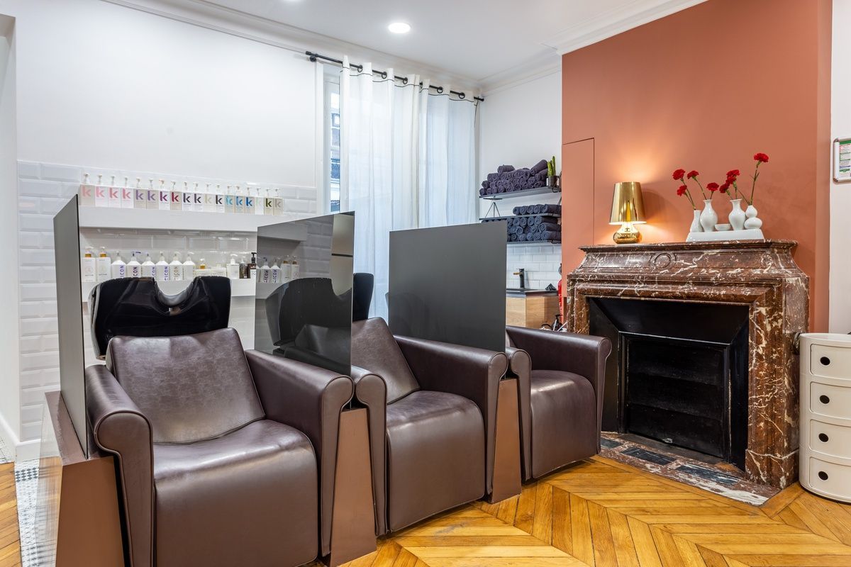 Intérieur d'un salon de coiffure avec chaises marron, miroirs et cheminée.