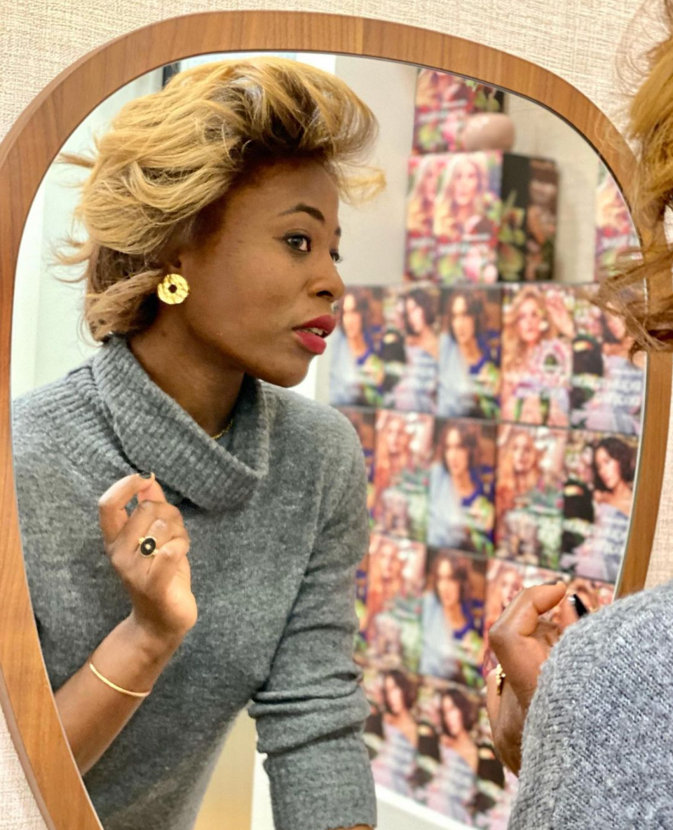 Femme se regardant dans un miroir, portant un pull gris, des boucles d'oreilles dorées