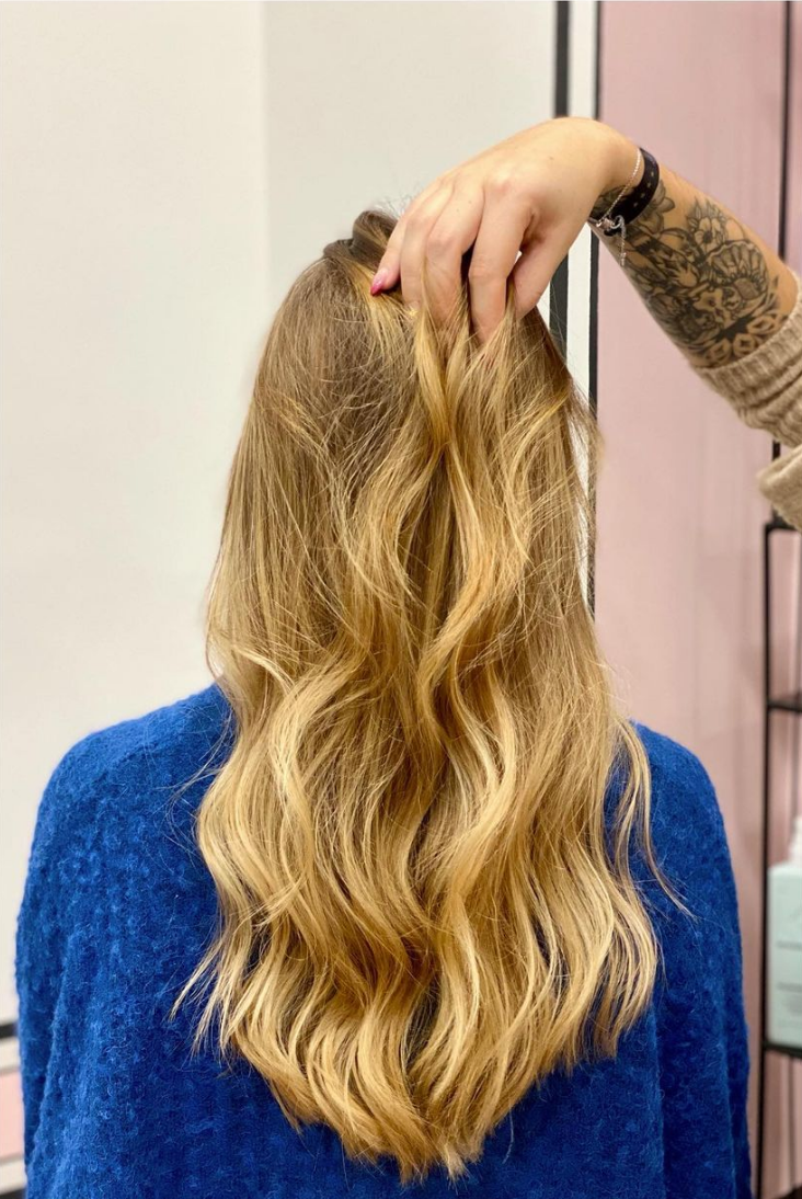 Une personne aux cheveux blonds ondulés, la main touchant ses cheveux.