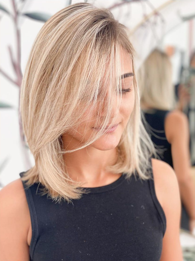 Femme avec une coupe au carré blonde dégradée, haut noir, regardant vers le bas.