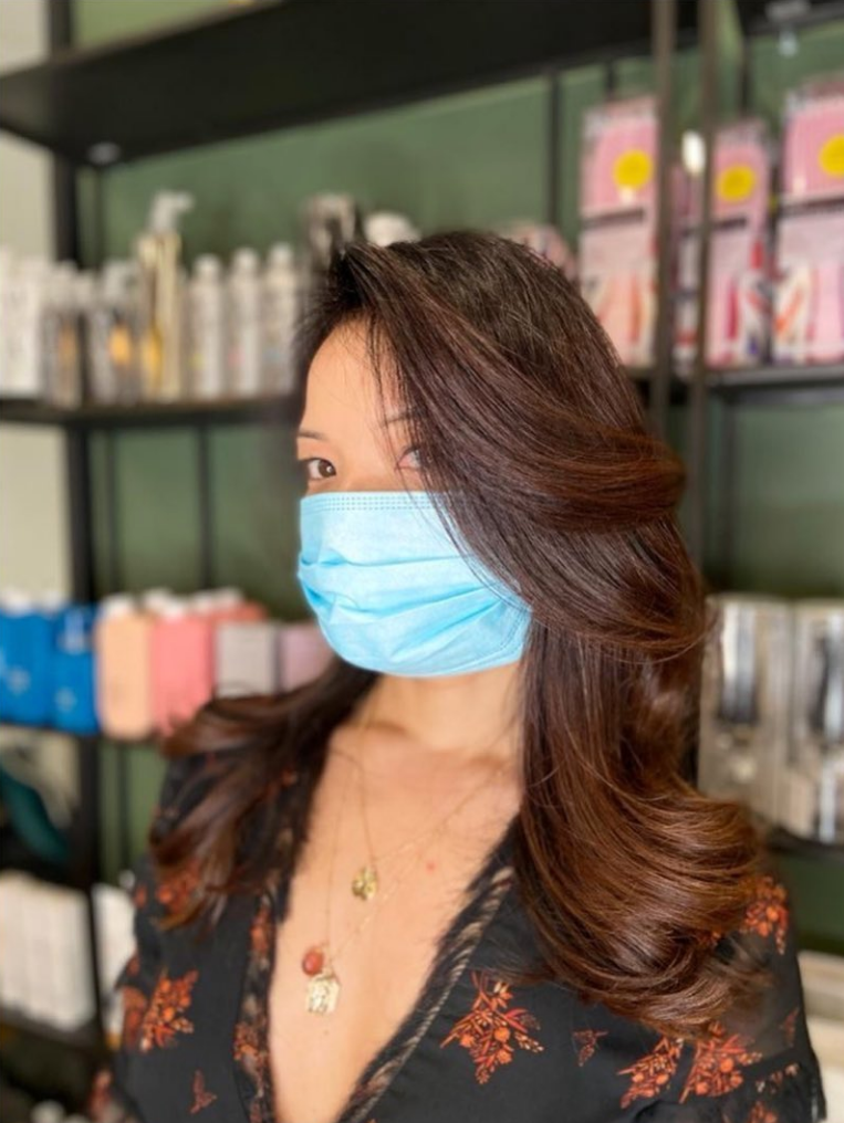 Femme aux longs cheveux bruns ondulés portant un masque bleu ; dans un salon de coiffure.