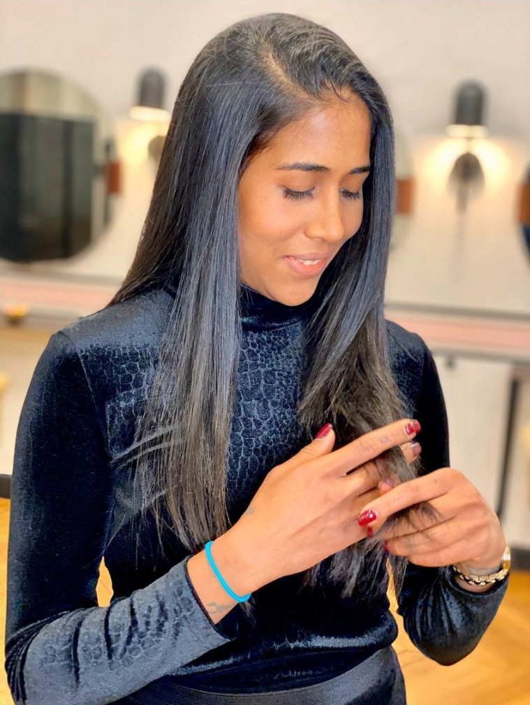 Femme en col roulé noir, regardant vers le bas, touchant une bague, avec de longs cheveux noirs.