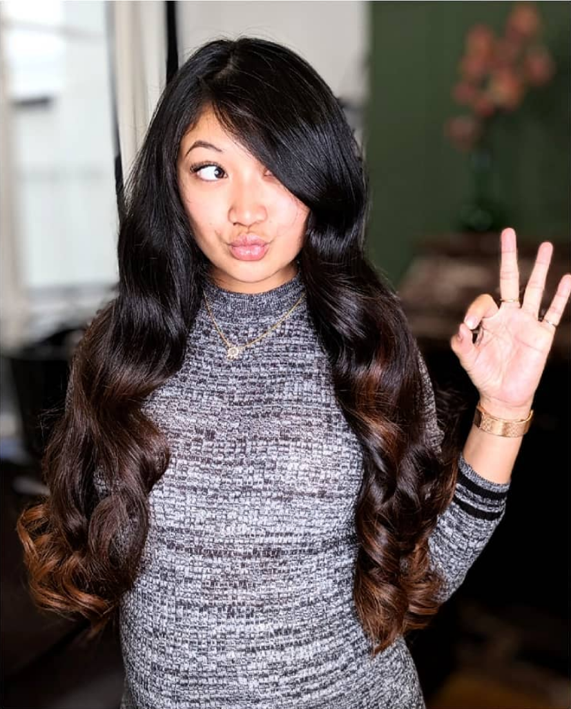 Femme aux longs cheveux ondulés et ombrés, faisant un geste « OK » et une moue boudeuse ; intérieur.