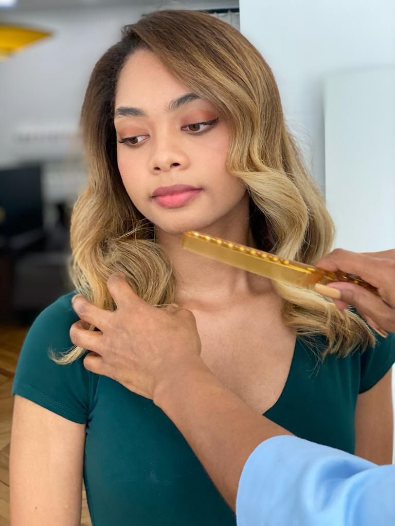 Femme blonde se faisant coiffer au peigne ; mains de la coiffeuse visibles. Chemise verte, expression neutre.