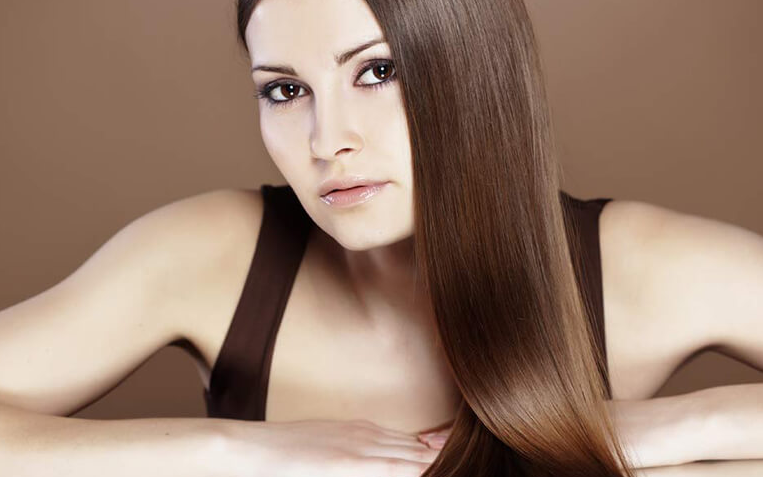 Femme aux longs cheveux bruns et raides, les bras posés sur une surface, le regard droit devant elle, expression neutre.