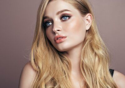 Femme blonde aux yeux bleus et au maquillage léger, regardant légèrement sur le côté avec une expression douce.