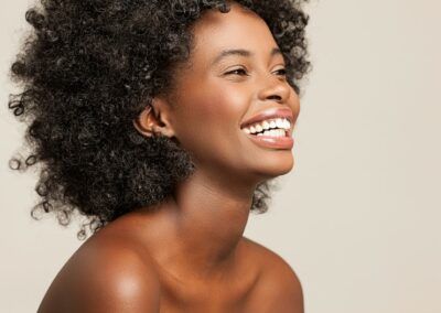 Une femme aux cheveux noirs et bouclés affiche un large sourire.
