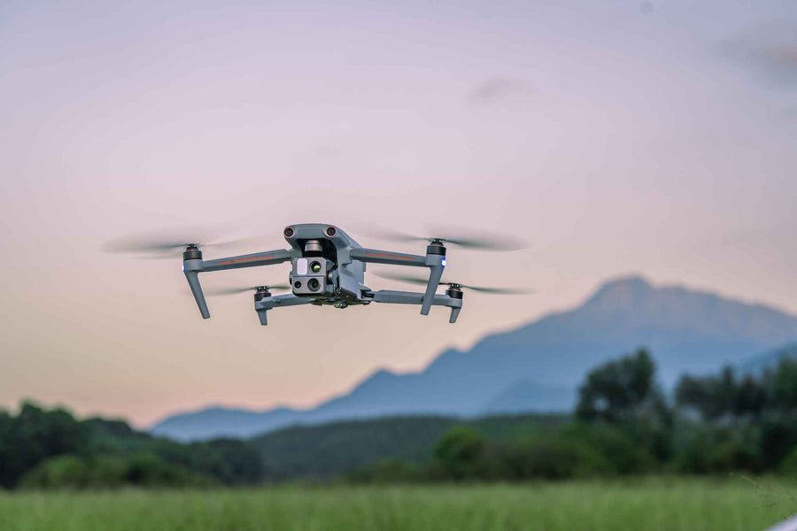 Drone flying over a green field with mountains in the background at dusk.