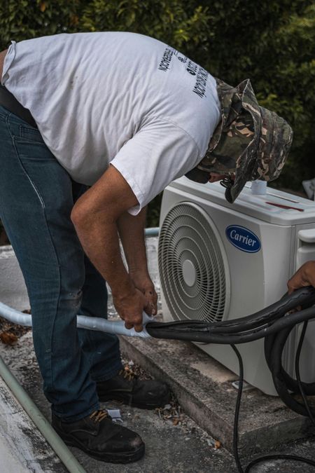Man in white shirt and camo hat installing an AC unit on a rooftop.