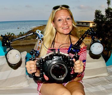 A lady with blonde hair holding a large underwater DSLR camera