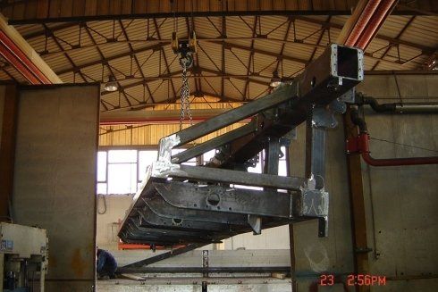 Un pesante componente industriale in acciaio sospeso tramite un paranco a catena all'interno di un'officina di fabbrica.