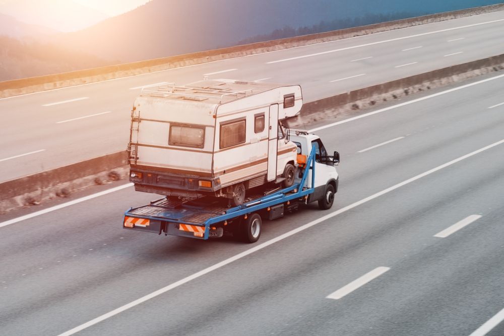 Tow truck carrying a white and beige RV on a highway.