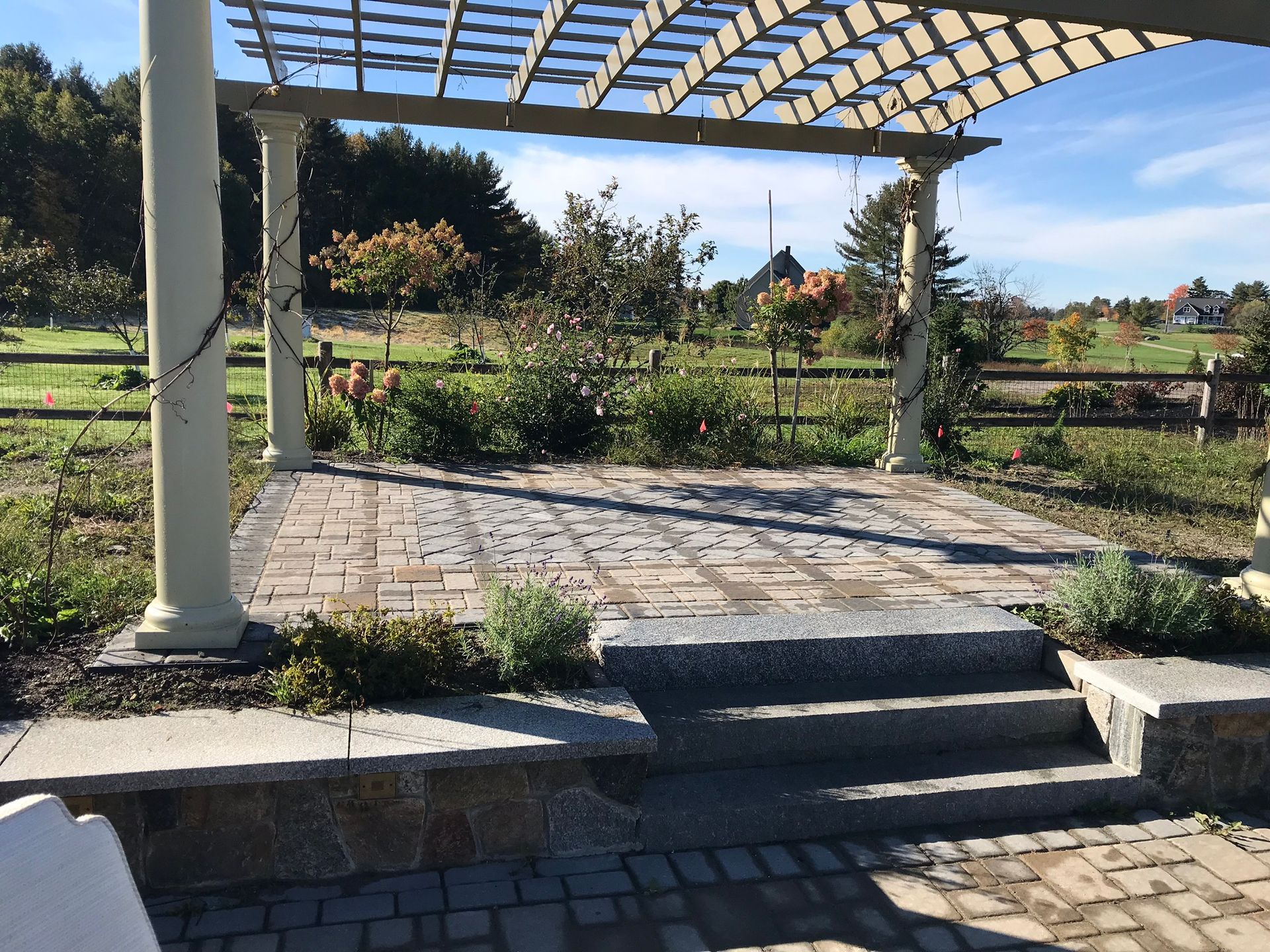 Stone patio with steps, pergola, and garden; sunny outdoor setting.