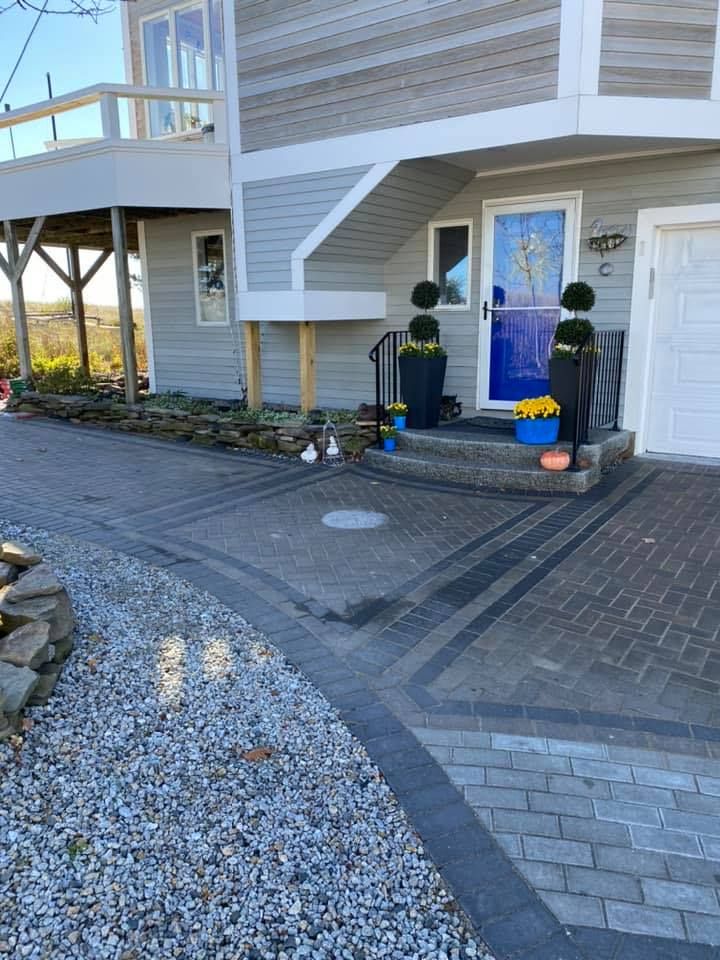 A gray house with a blue door and paver driveway with landscaping and topiaries.