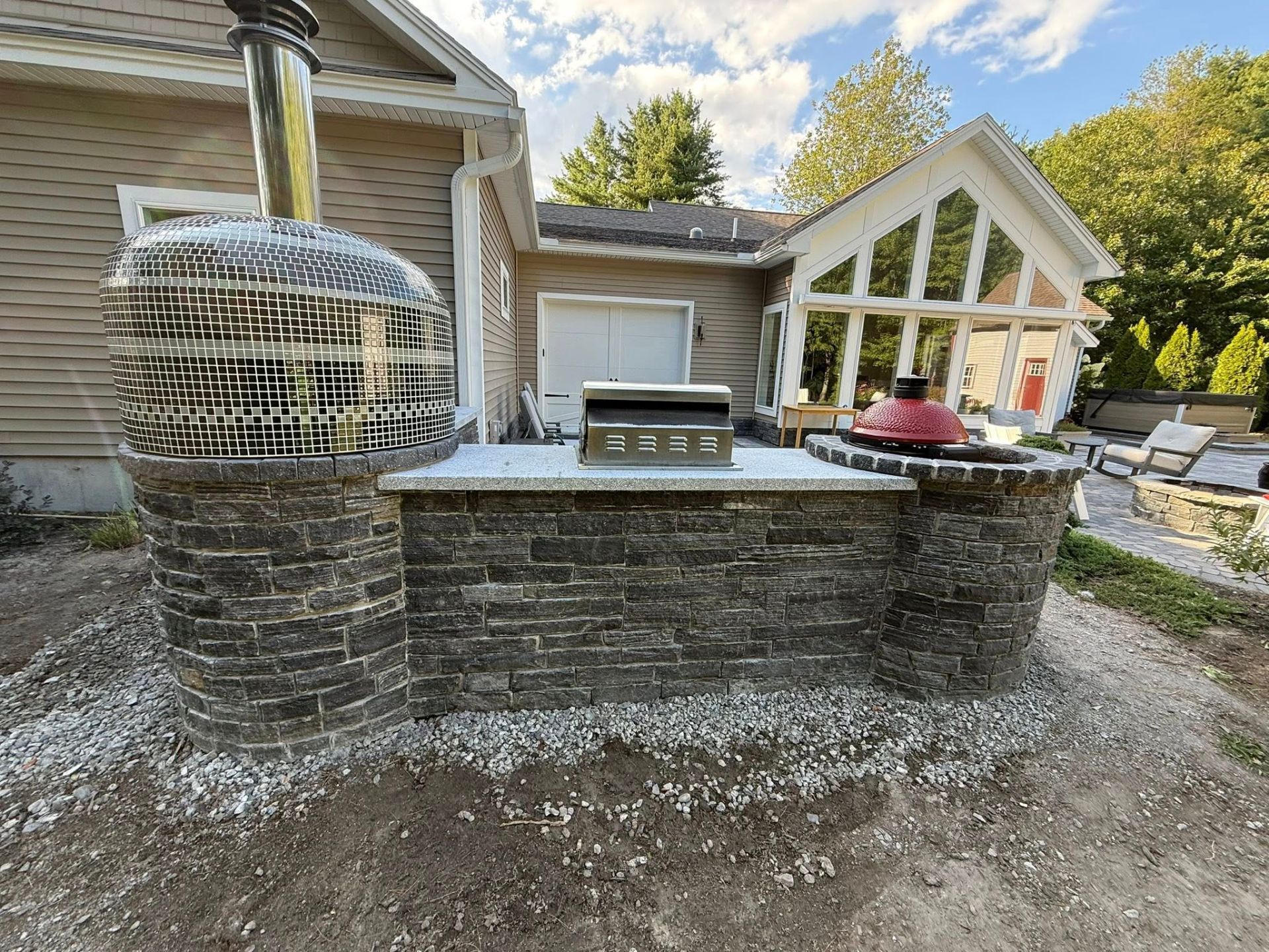 Outdoor kitchen with brickwork, a grill, pizza oven, and a scenic backdrop.