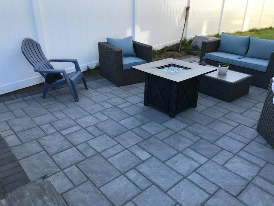 Patio with gray pavers, wicker furniture, and a fire pit, next to a white fence.