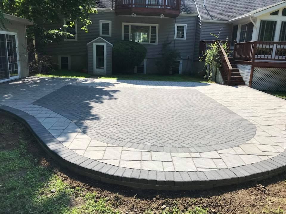 Brick patio in a backyard. Gray pavers with a curved border. Grass surrounds the patio.