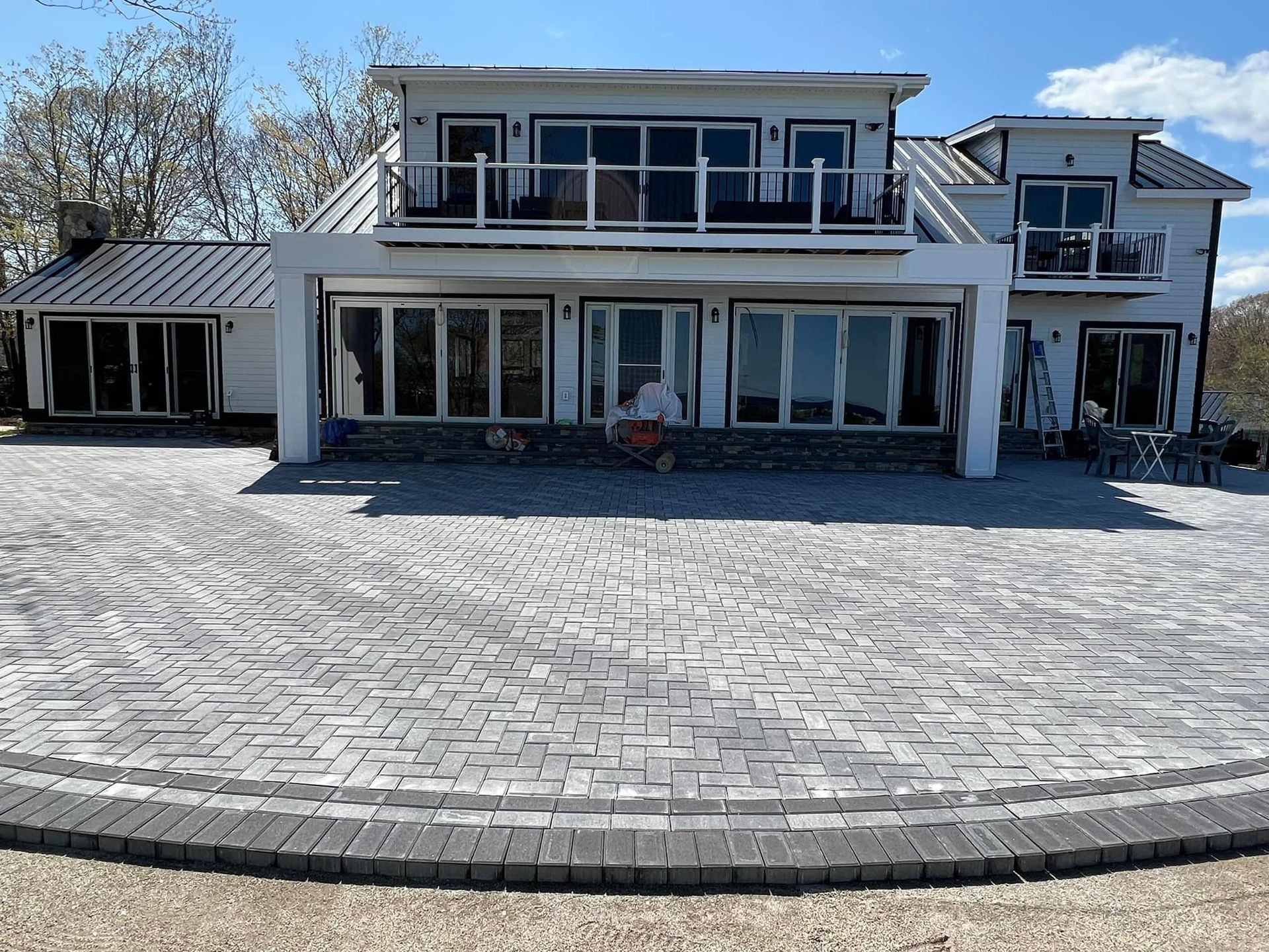 A white modern house with a large brick patio. A person is sitting in front of the house.
