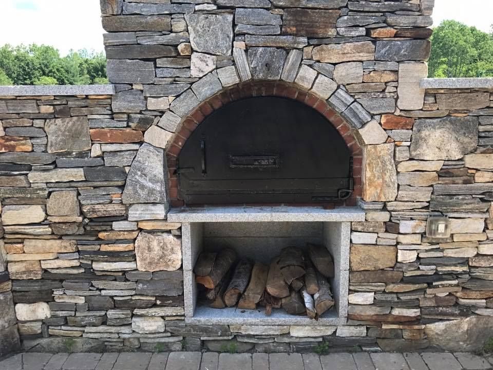Stone outdoor pizza oven with firewood storage below.