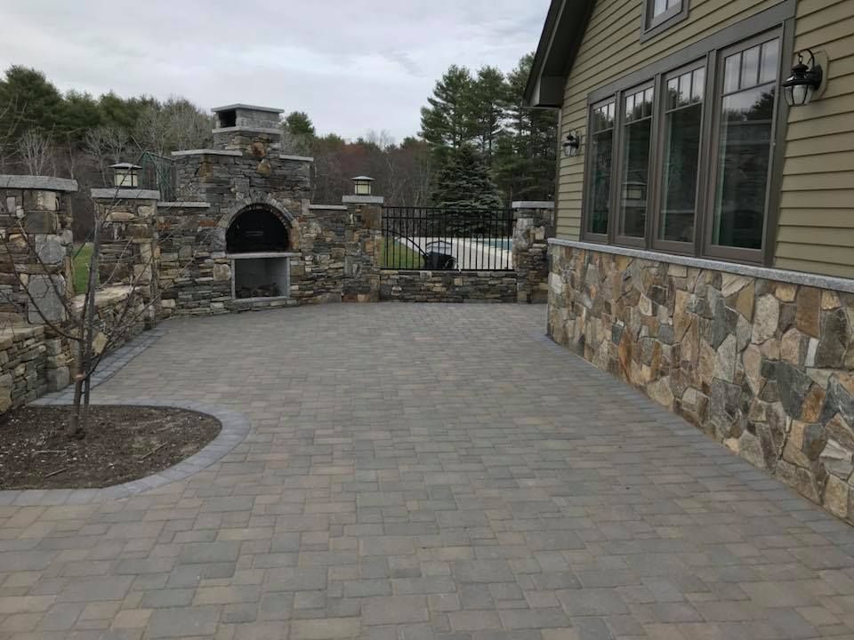 Stone patio with a pizza oven, next to a house with stone siding.