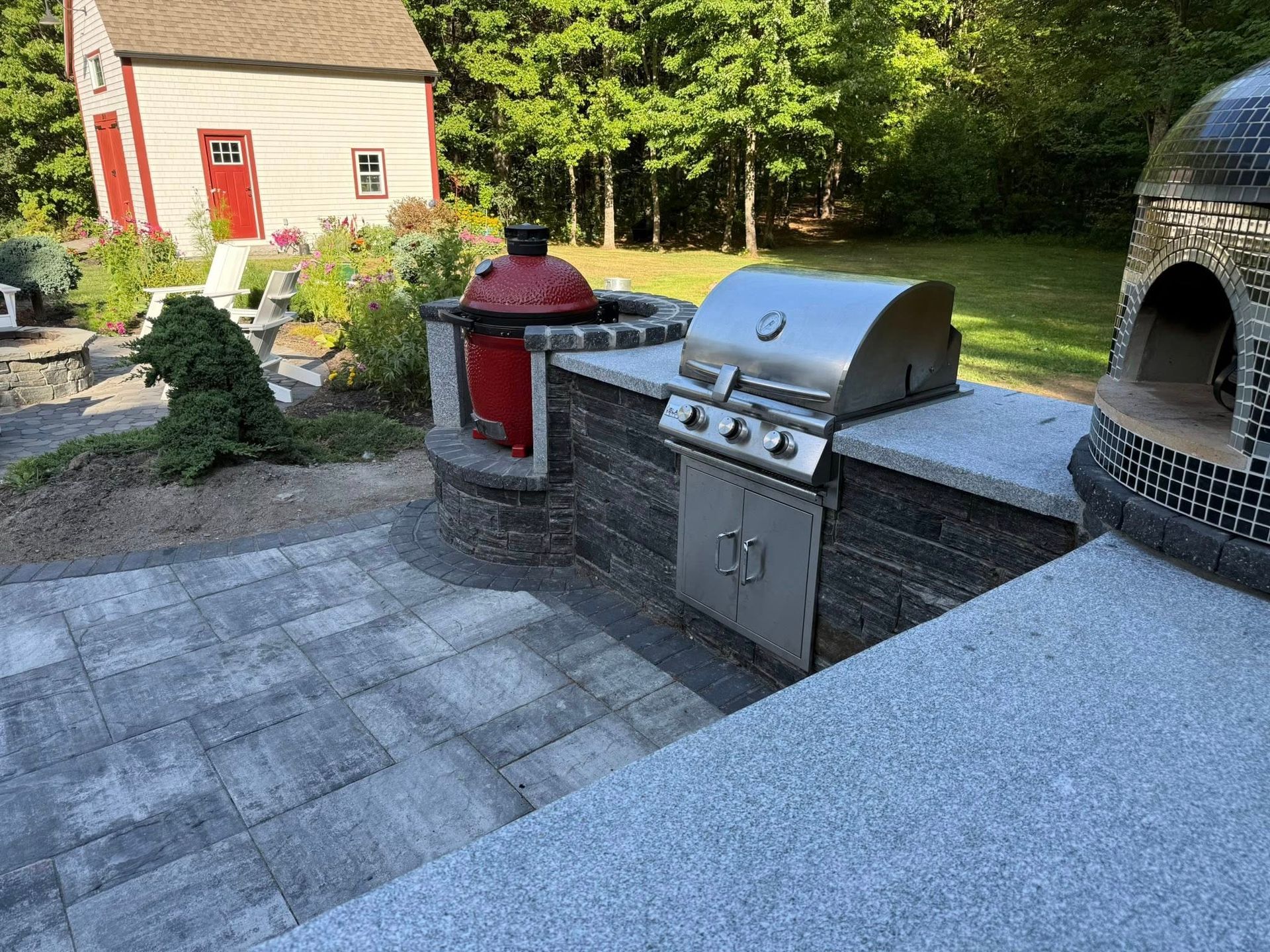 Stone patio with built-in grill, smoker, and pizza oven, in backyard with a small shed.