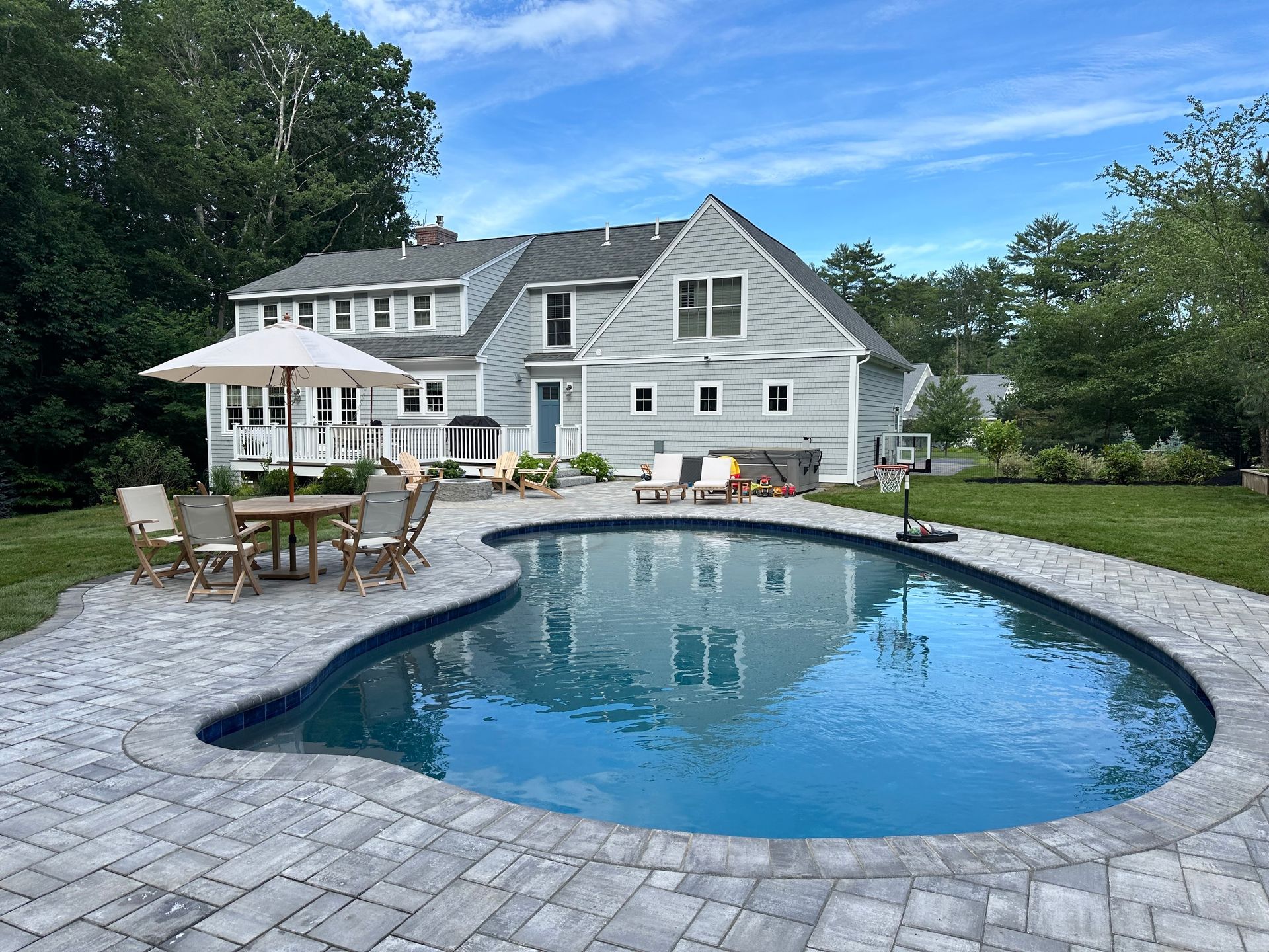 A backyard with a pool, patio furniture, and a grey house on a sunny day.