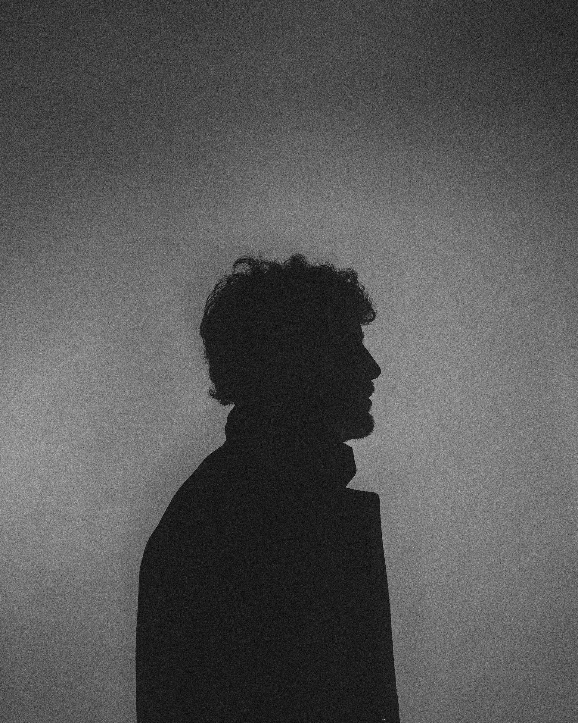 A black and white photo of a silhouette of a man standing in front of a wall.